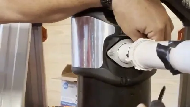 Hands attaching a white drain pipe to the outlet of a garbage disposal under a sink