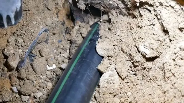 Black pipe with a green stripe lying exposed in a dirt trench