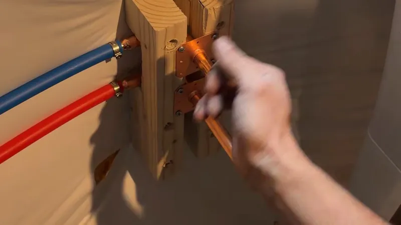 A hand adjusting blue and red PEX tubing connections mounted on a wooden block