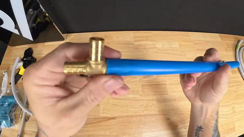 Hands holding blue PEX tube fitted with a brass tee over a wooden table