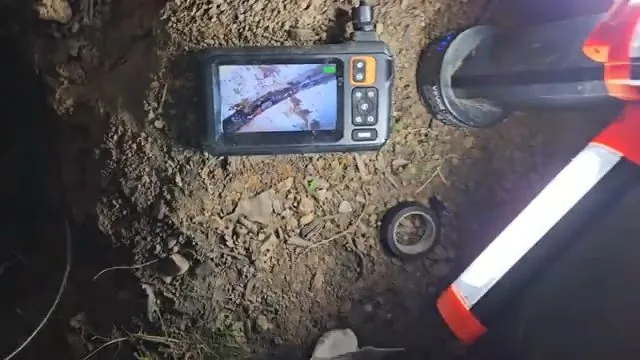 An inspection camera monitor resting on dirt next to a pipe in an excavation