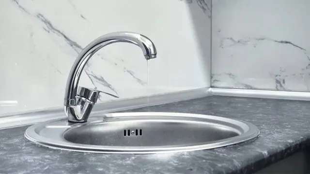 A chrome kitchen faucet running water into a round steel sink with a marble backsplash