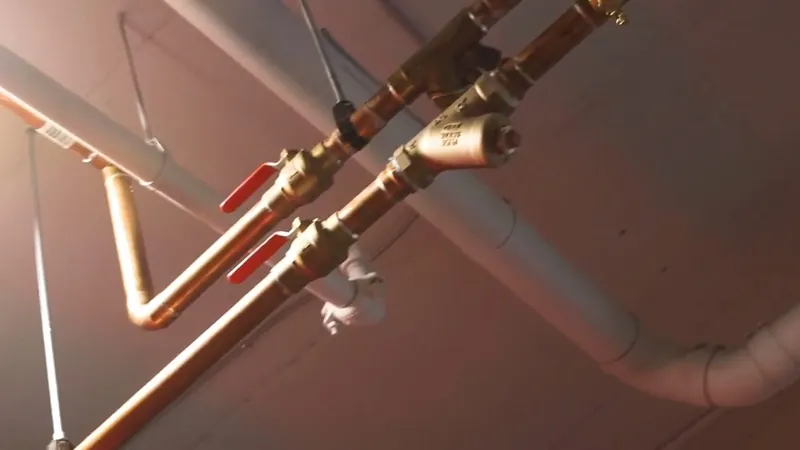 Copper pipes with red ball valves running along a ceiling beside a white pipe