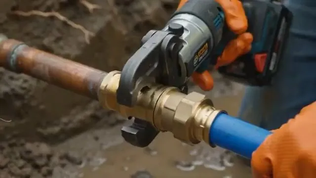 Orange-gloved hands crimping a brass fitting that joins copper pipe to blue PEX in a dirt trench