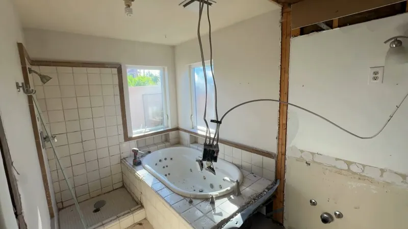 A demolished bathroom with the tub and shower tile still in place and the walls opened up