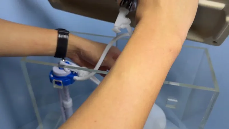 A forearm wearing a watch reaching into a toilet tank to work on the fill valve