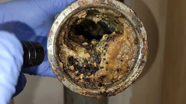 A gloved hand holding a corroded drain pipe section while a flashlight shines inside it