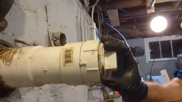 Gloved hands opening a cream-coloured cleanout cap in a basement