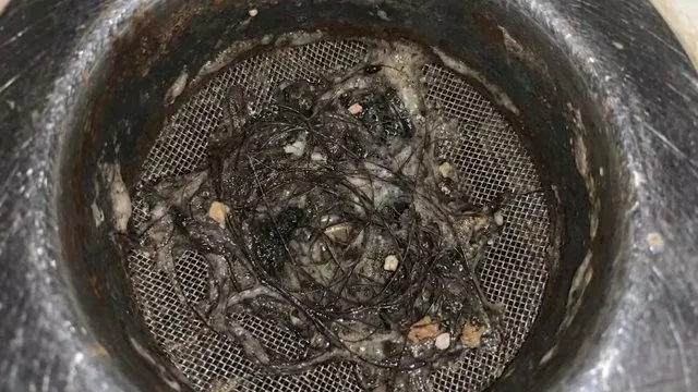 A dark drain basket strainer packed with hair and debris, seen from above