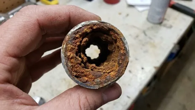 A hand holding a rusted pipe section with its interior mostly blocked by scale