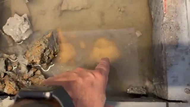 A hand pointing at a wet, damaged area in a concrete slab