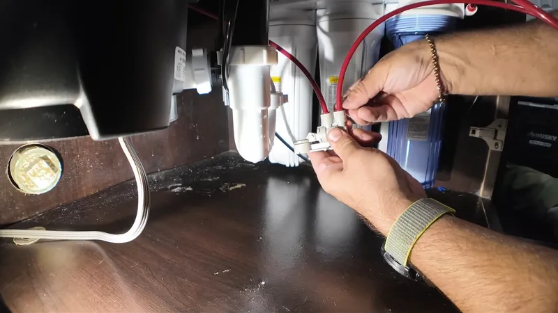 Hands connecting wires under a sink next to a garbage disposal unit