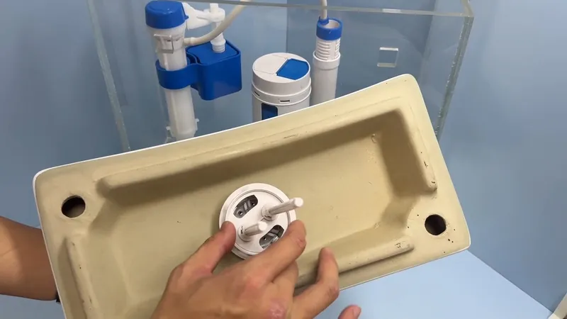 Hands holding a toilet tank lid while two fill valves stand behind it