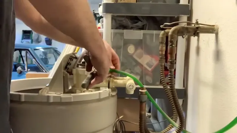 Hands working on a water softener control valve and green tubing