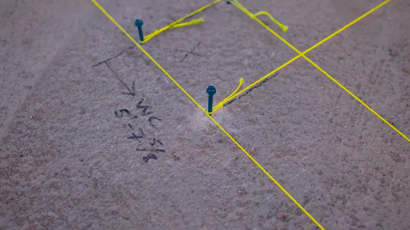 A concrete slab marked with yellow string lines, blue pins and handwritten notes