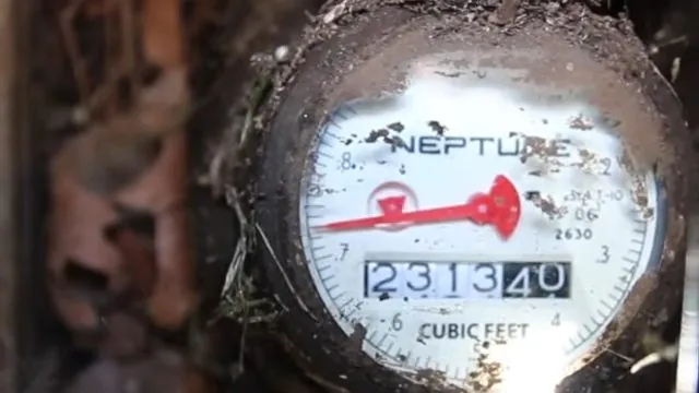 A water meter dial inside a dirty ground-level meter box