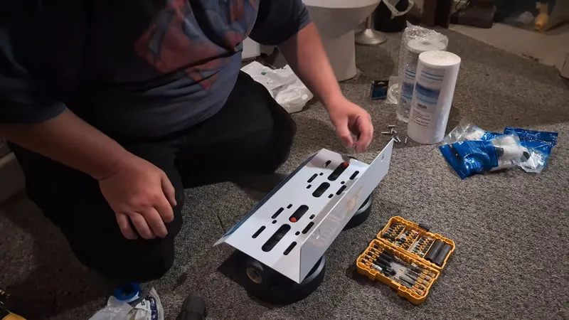 A person kneeling on the floor assembling a mounting bracket with filter cartridges and tools