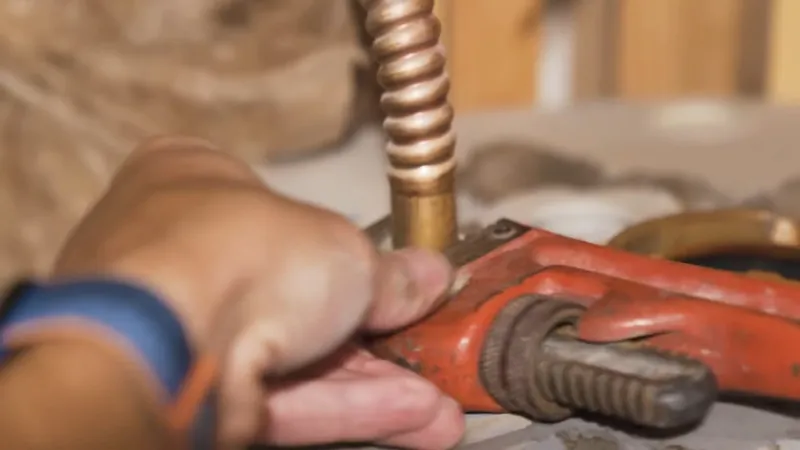 A hand using a red pipe wrench on a corrugated copper water heater connector