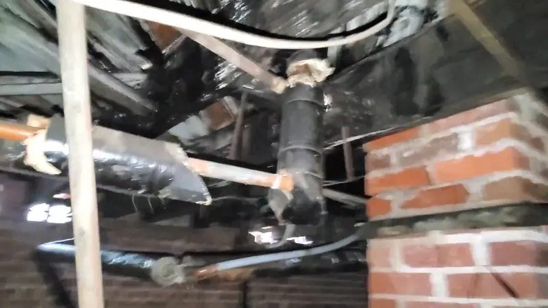 Dark pipes and insulation in a crawlspace beside a brick pier