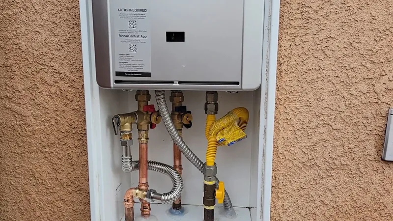 A tankless water heater set in a wall recess on an orange stucco wall, with pipes and valves below