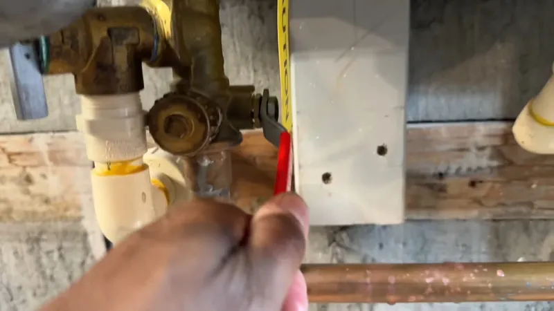 A hand holding a tape measure beside tankless heater piping and a brass valve