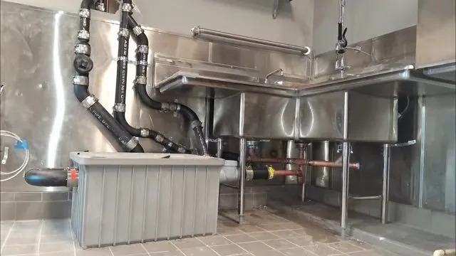 A commercial kitchen three-compartment sink with piping and a grease trap beneath