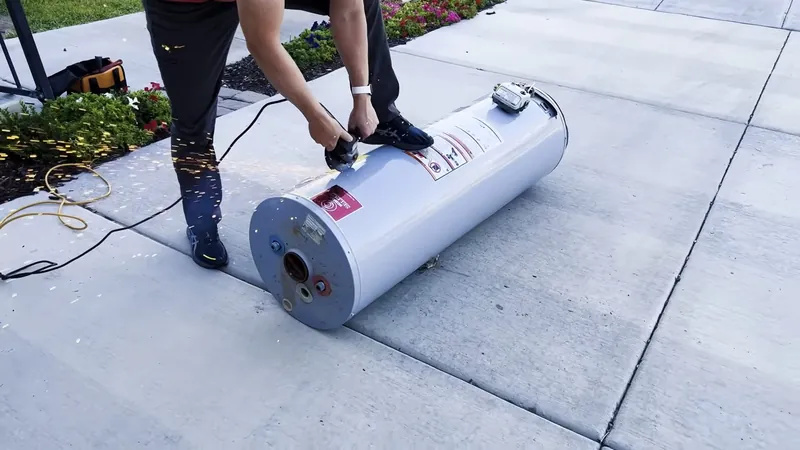 Two people moving a water heater lying on a hand truck across a patio