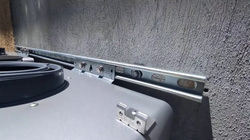 The top edge of a gray water heater tank with a metal rail bracket mounted on the wall behind it