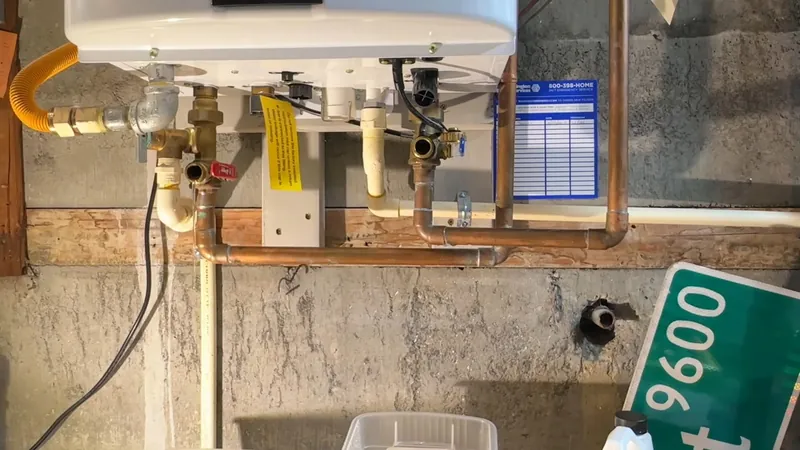 A wall-mounted tankless water heater with copper pipes, valves and a gas line, and a green sign at the corner