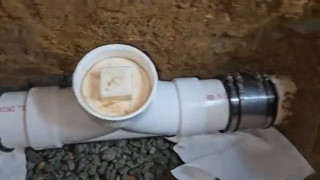 A white PVC cleanout tee with its cap in place in a dirt trench